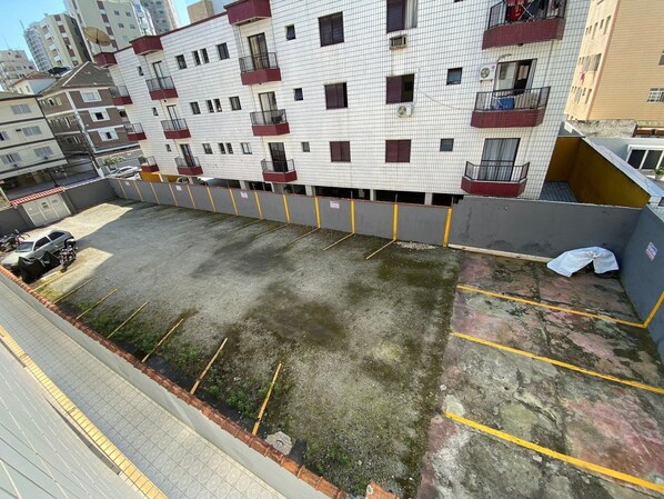 Un immeuble résidentiel à plusieurs étages doté de balcons, d’un espace de stationnement avec des places délimitées et d’une entrée sécurisée par un portail.