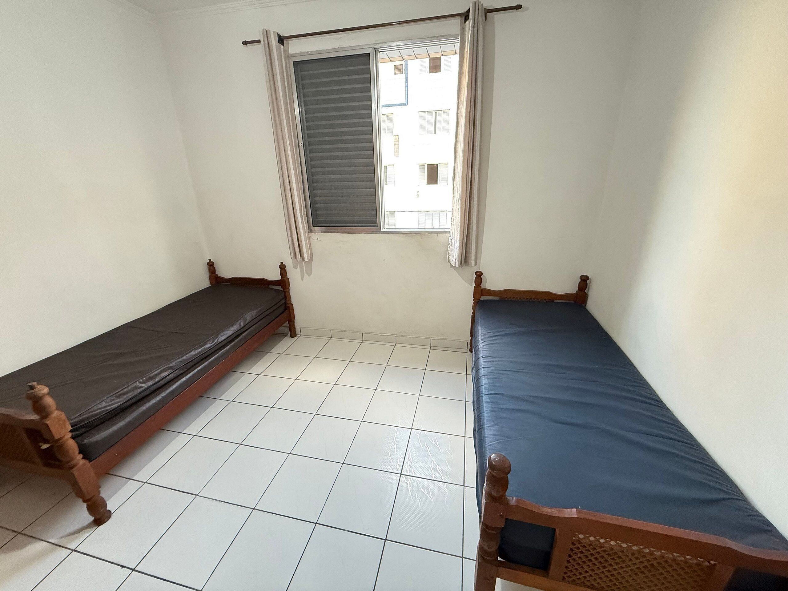 A small, clean room with two wooden beds, a tiled floor, and a window with curtains.