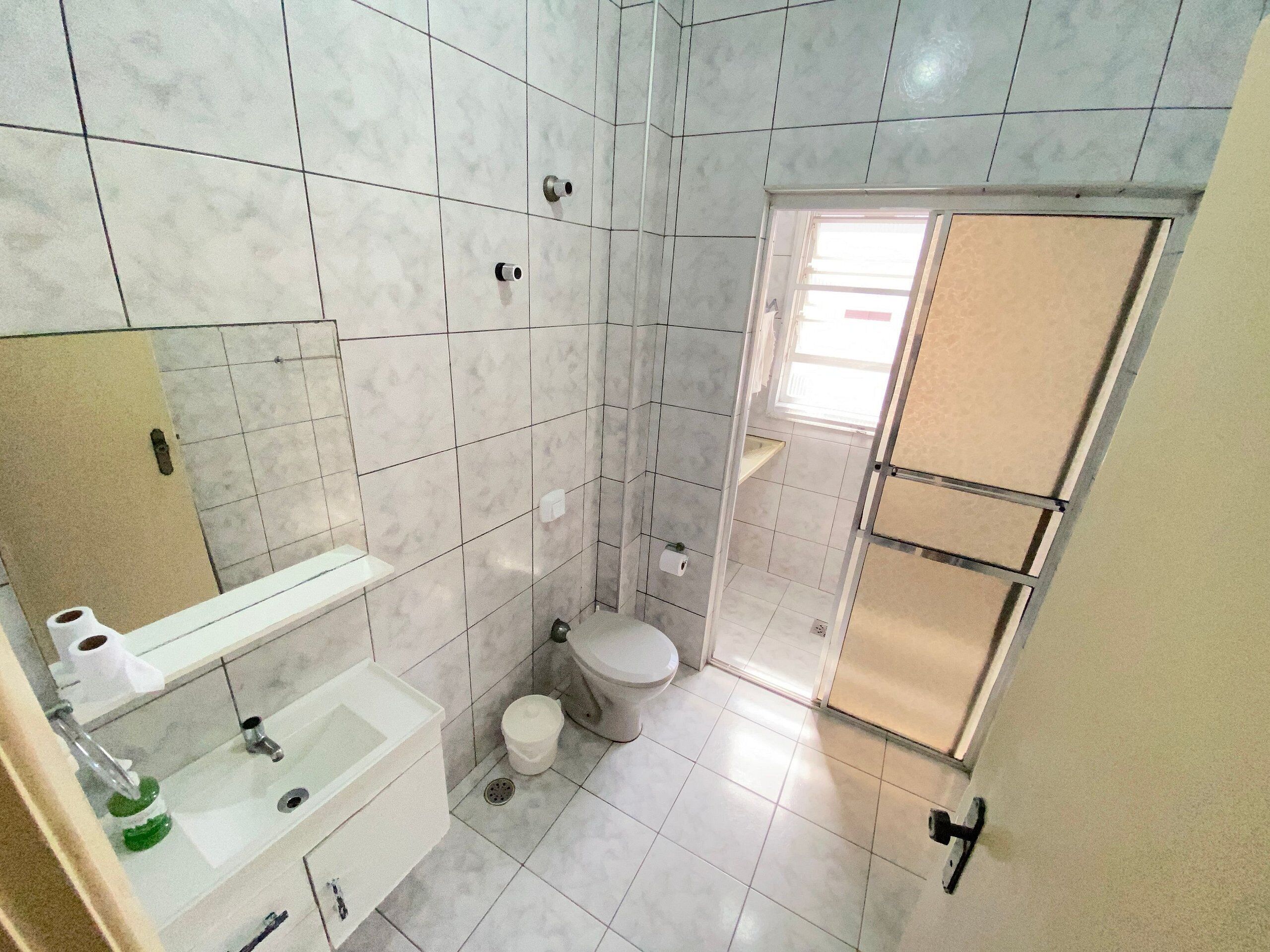 A small bathroom with a toilet, sink, and mirror. There is a window providing natural light.