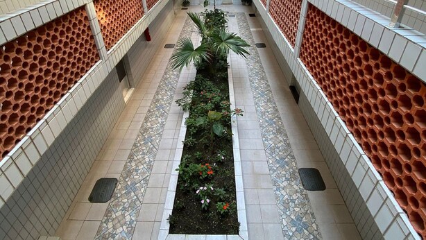 Un atrium à plusieurs niveaux, doté de sols carrelés, d’un jardin central agrémenté de plantes et de rampes en treillis rouge.