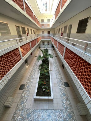 Un atrium à plusieurs niveaux, doté de sols carrelés, d’un jardin central agrémenté de plantes et de rampes en treillis rouge.