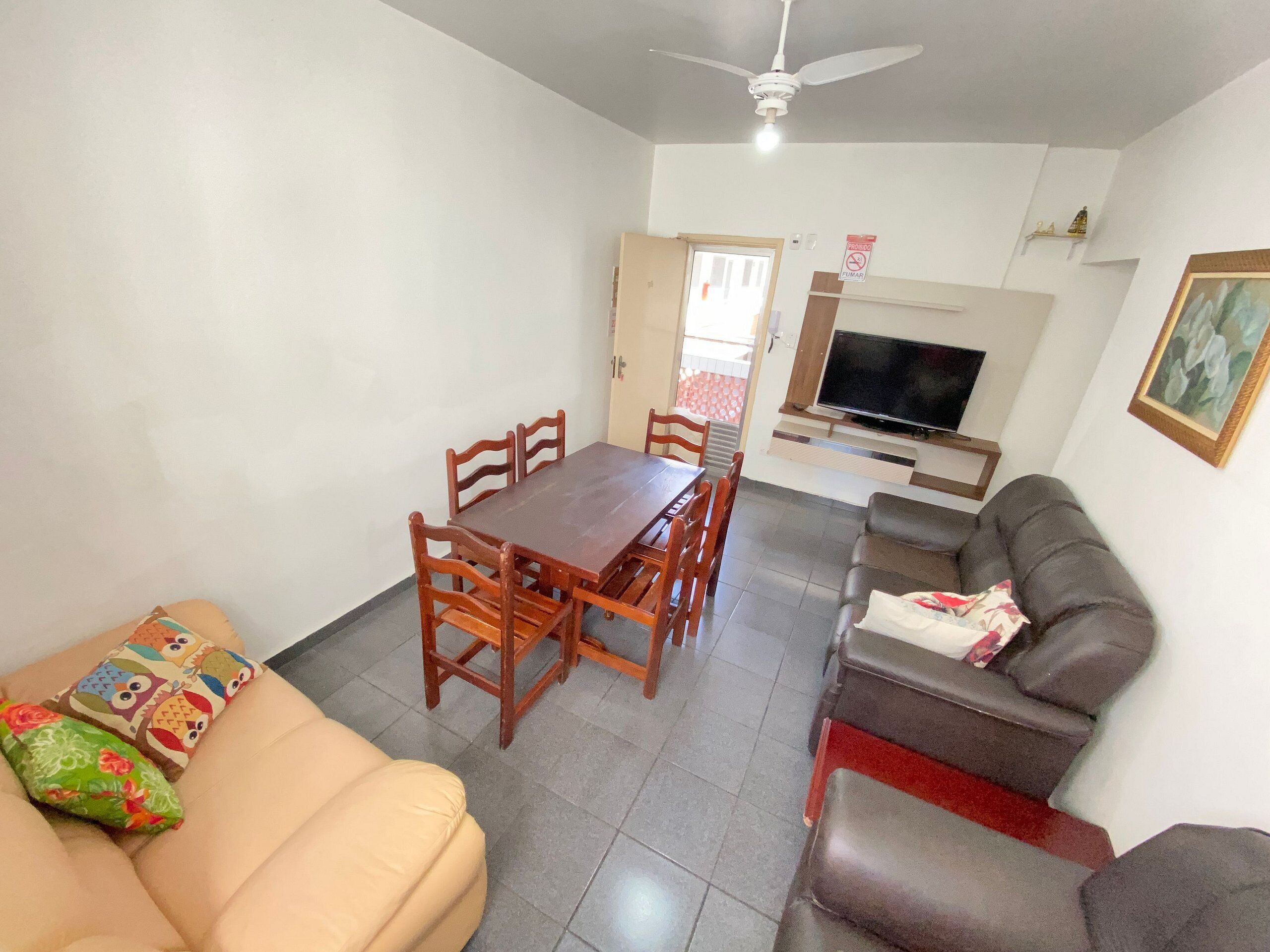 A living room with a sofa, a dining table with chairs, a TV, and a ceiling fan.