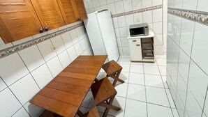 Une cuisine avec des murs recouverts de carreaux blancs, des meubles de cuisine en bois, un réfrigérateur blanc, un four à micro-ondes et une table à manger en bois avec des chaises.