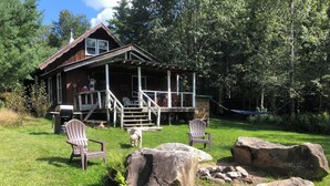 A rustic cabin with a porch, outdoor seating, and a grill area.