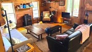 A cozy cabin interior with a wooden interior, a sofa, a coffee table, a chair, a television, and a fireplace.