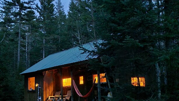 A rustic cabin with a porch, wooden deck, and a hammock.
