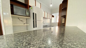 A kitchen with granite countertops, a microwave, and a refrigerator. - Pé na areia Canto do Forte III (Praia Grande)