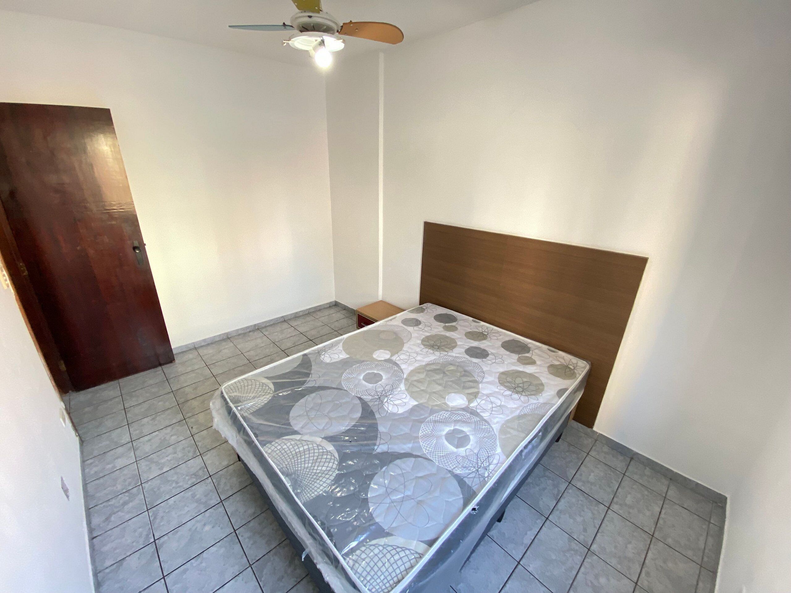 A small, clean room with a bed, a wooden door, and a ceiling fan.