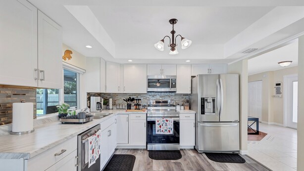 A modern kitchen with white cabinets, stainless steel appliances, and a wooden floor. - Charming 3-bedroom house with Heated pool/3 mins Sister Spring (Crystal River)