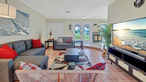 A living room with a grey sofa, red and white cushions, a black coffee table, and a large flat-screen TV. - Charming 3-bedroom house with Heated pool/3 mins Sister Spring (Crystal River)