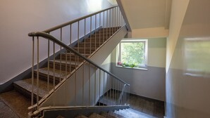 A staircase with metal railings, a window with a view of trees, and a small potted plant on the windowsill. - Uniwersytecka Standard Studio (Lódz)