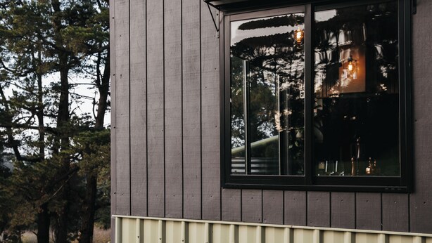 Un bâtiment moderne doté d’une grande fenêtre qui reflète les arbres et d’un luminaire.