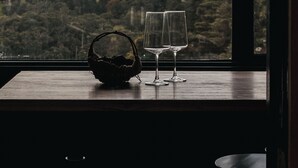 Une vue à travers une fenêtre, avec une table en bois, deux verres à vin et un panier.