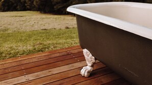 Une baignoire sur une terrasse en bois, avec une zone herbeuse et des arbres en arrière-plan.