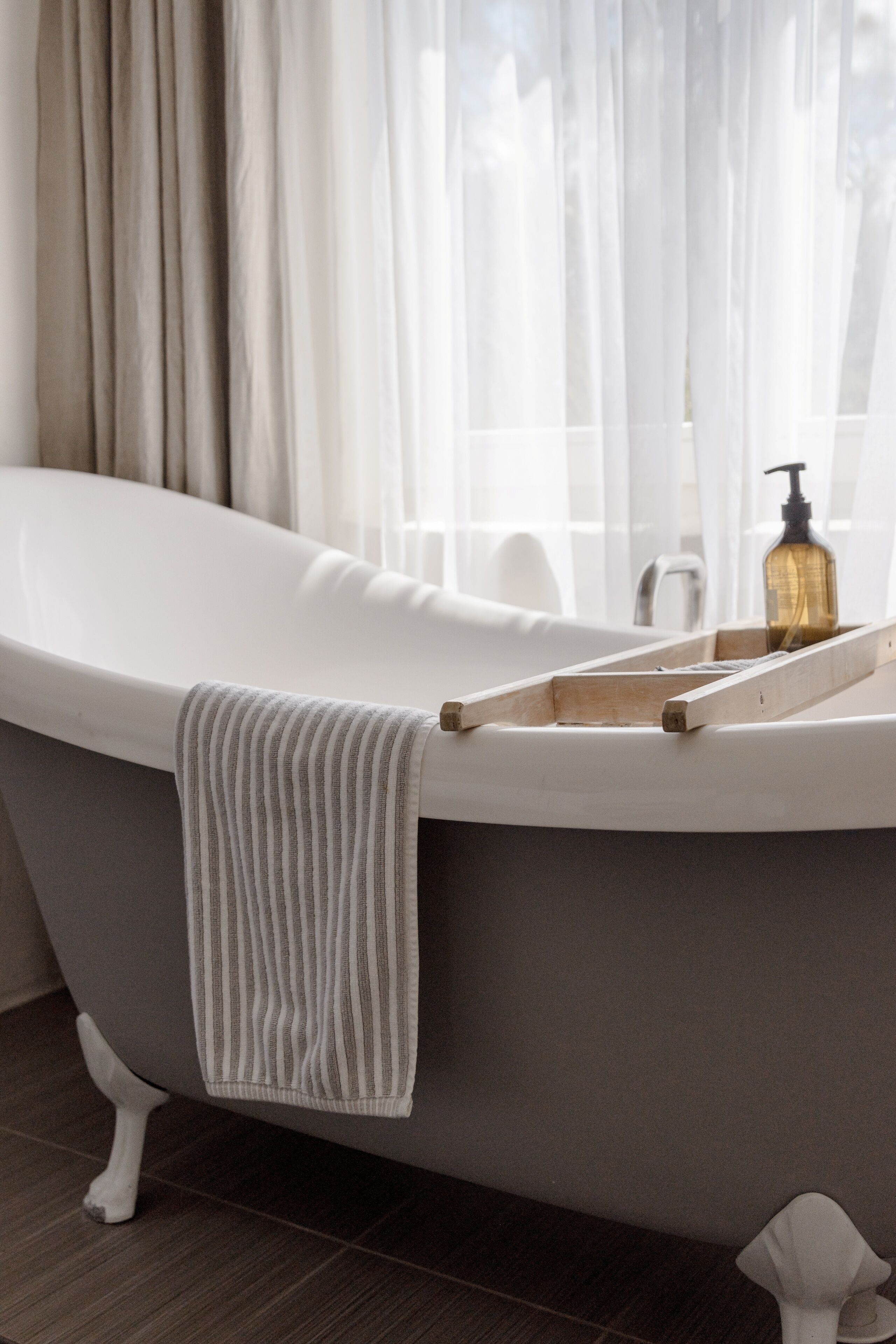 Een moderne badkamer met een vrijstaand bad, een houten dienblad en een zeepfles.