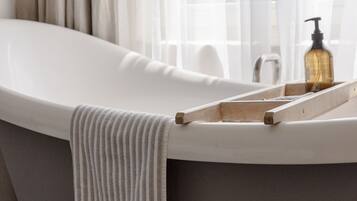 Een moderne badkamer met een vrijstaand bad, een houten dienblad en een zeepfles.