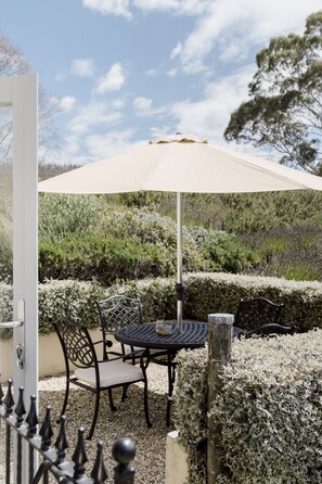 An outdoor seating area with a table and chairs under a canopy, surrounded by neatly trimmed hedges and a clear sky. - French Fields NZ (Fairhall)