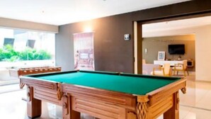Una mesa de billar en una habitación bien iluminada de diseño moderno, una puerta que da a otra zona y vistas al exterior.