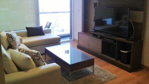 Una sala de estar con un sofá, una mesa de centro, un televisor y un ventanal grande.