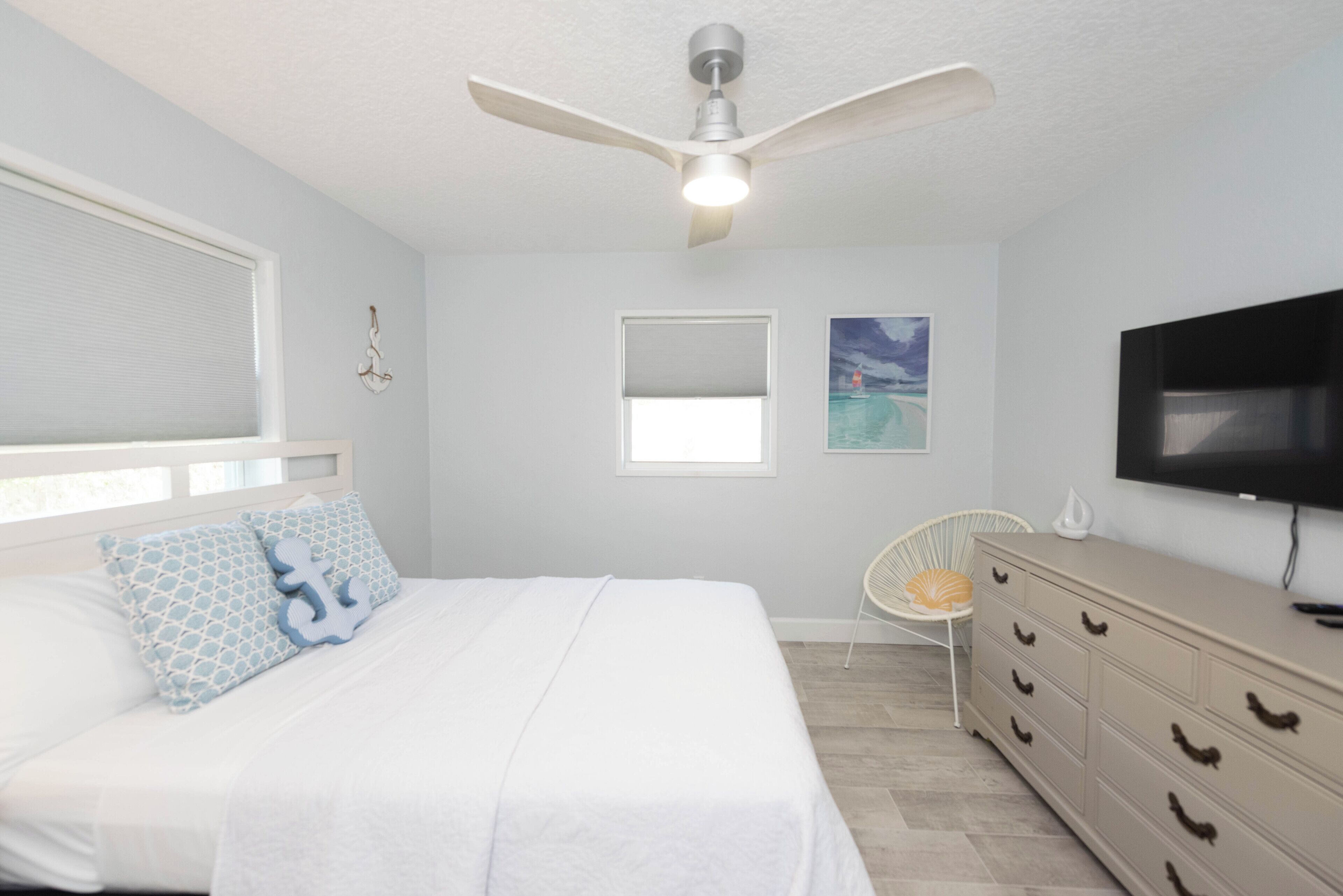 A bedroom with a bed, a ceiling fan, a TV, a dresser, and a window with blinds.