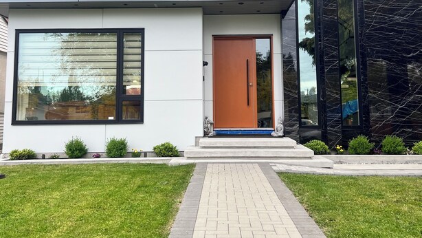 Una casa moderna de dos pisos con ventanas amplias, una entrada central con puerta de madera y un camino de entrada pavimentado.