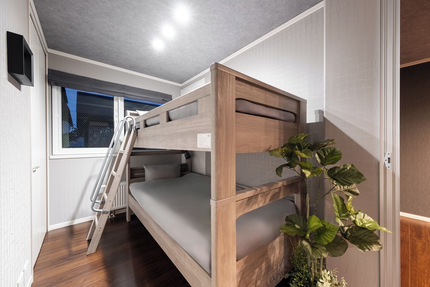 A bunk bed room with a wooden ladder, a window with a view, and a plant.