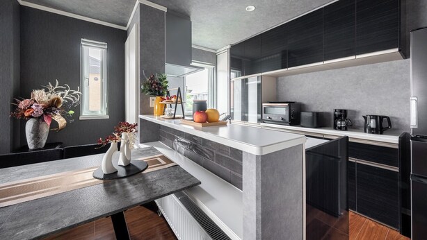 Une cuisine moderne avec des meubles de couleur sombre, un îlot central et un coin repas comprenant une table et des chaises.