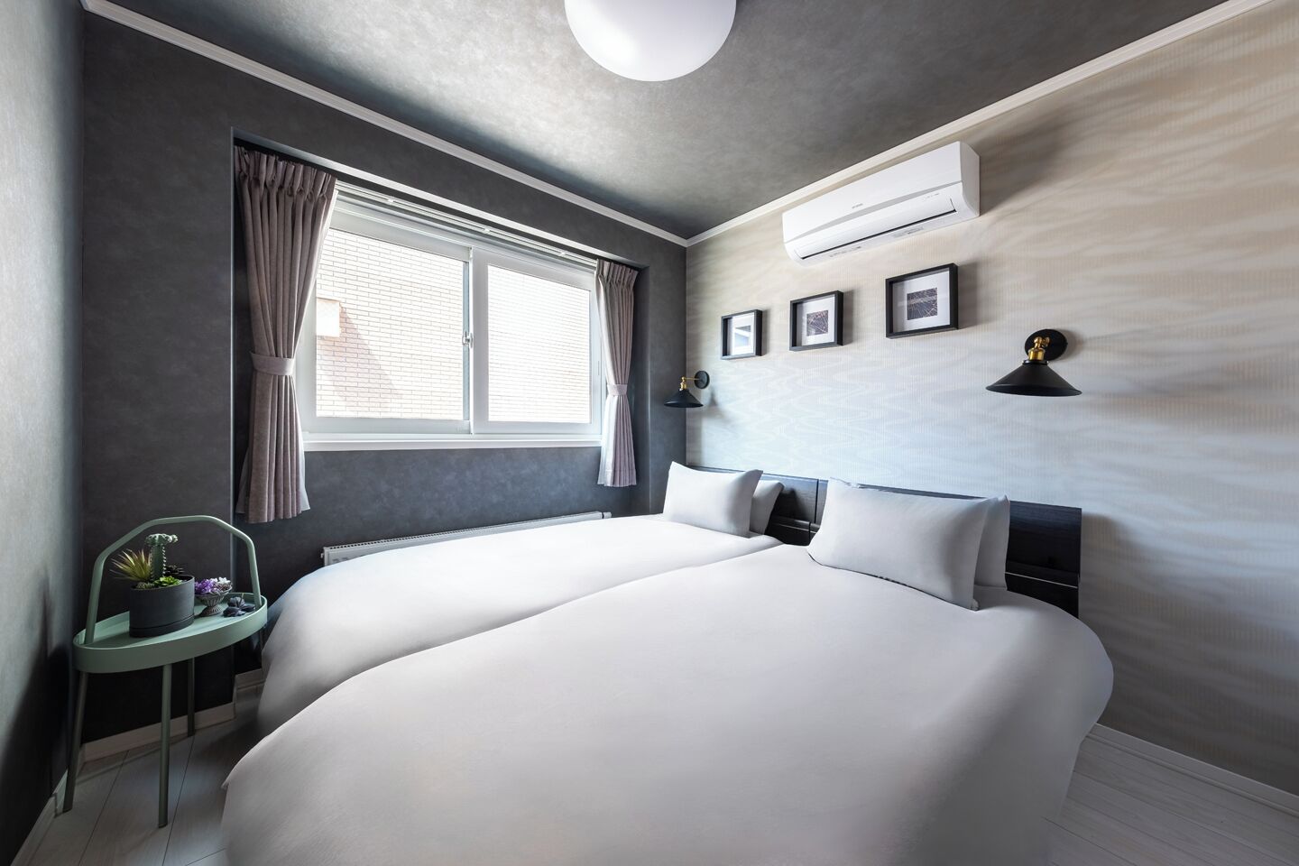 Una habitación de hotel moderna con una cama grande, una mesita de noche con una planta, una ventana con cortinas y un equipo de aire acondicionado en la pared.