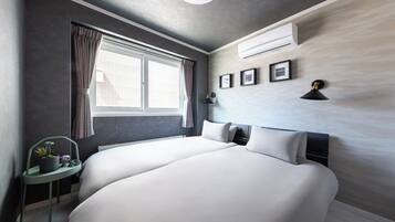 Una habitación de hotel moderna con una cama grande, una mesita de noche con una planta, una ventana con cortinas y un equipo de aire acondicionado en la pared.