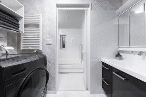 A modern bathroom with a built-in washer and dryer, a shower, and a vanity with a mirror. - THE EXEPAREL (Kushiro)