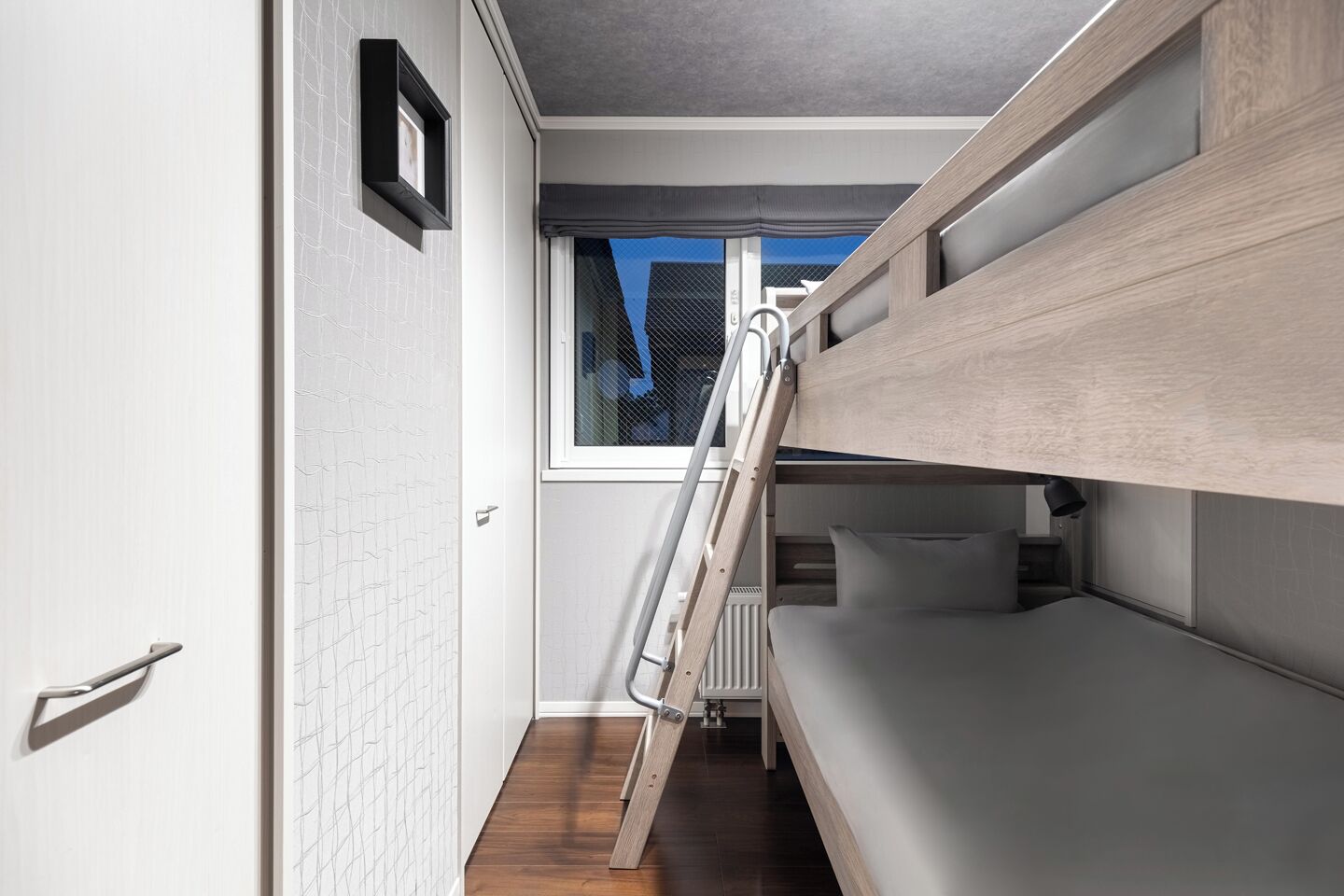 A compact room with a bunk bed, a ladder, a window, and a white door.