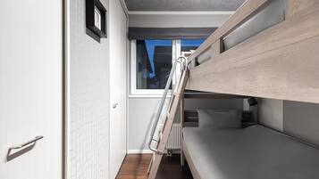 A compact room with a bunk bed, a ladder, a window, and a white door.