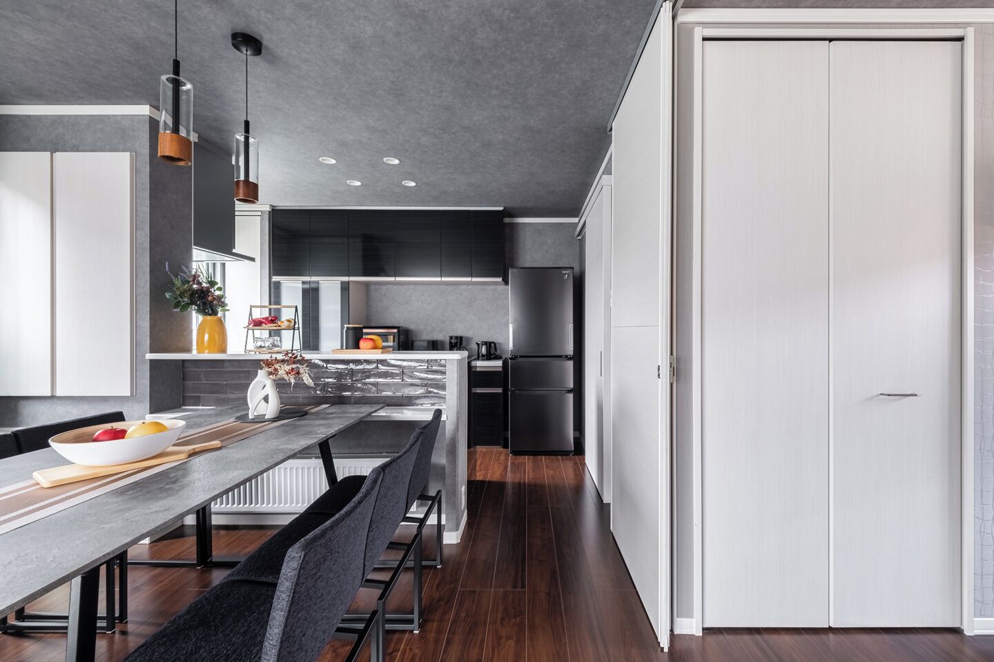 A modern kitchen with a long island, dark cabinets, and a white door.