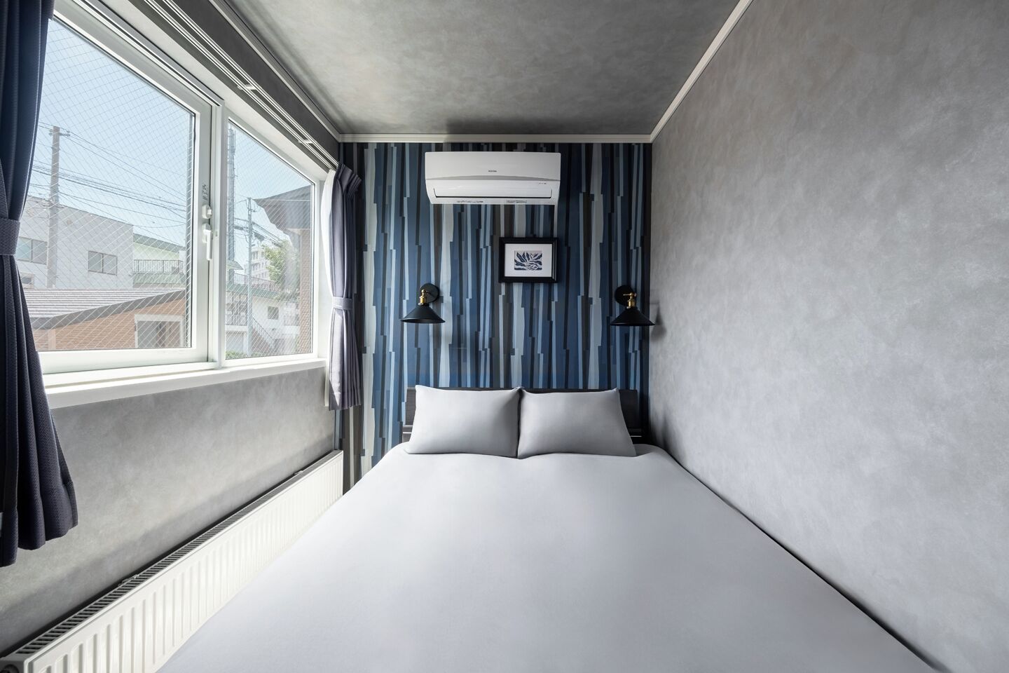 A hotel room with a bed, a window, an air conditioning unit, and striped wallpaper.