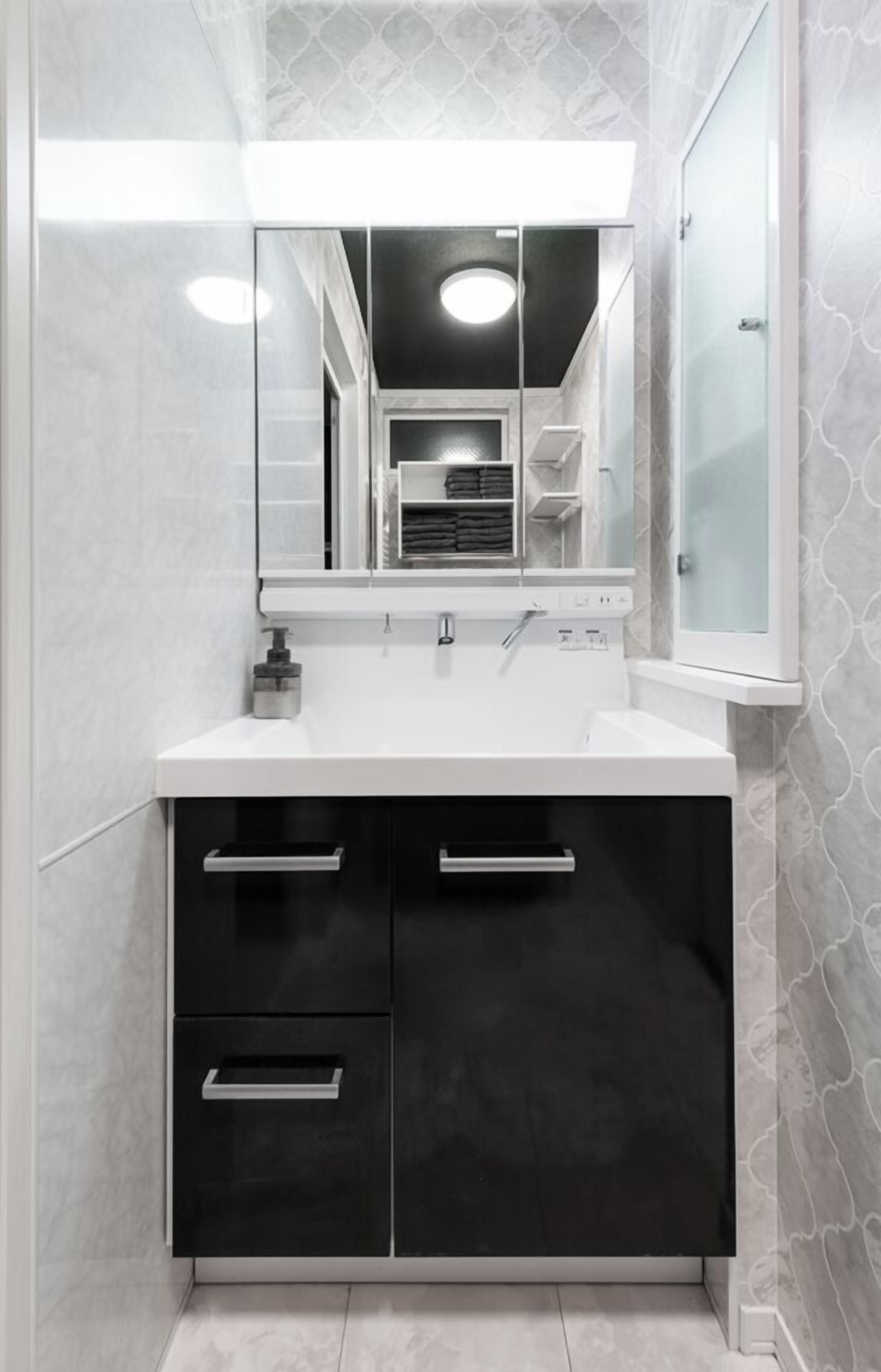 A modern bathroom with a white sink, black cabinets, and a large mirror.