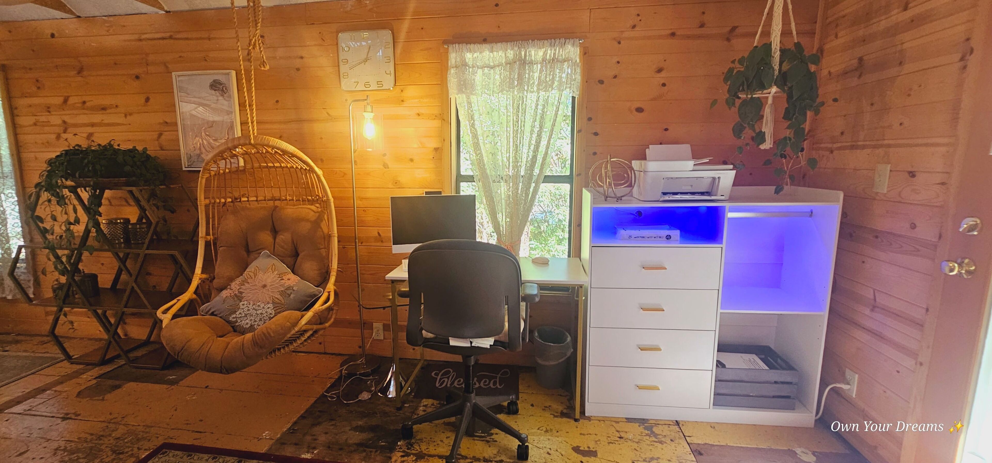 A cozy room with a wooden interior, a hanging chair with cushions, a desk with a computer, and a printer on a shelf.
