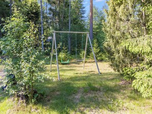 Une balançoire installée dans un espace boisé, avec de l’herbe et des arbres.
