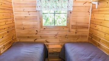 A cabin room with two beds, a window with a lace curtain, and a small wooden nightstand.