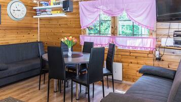 Een knus chaletinterieur met een eettafel, stoelen, een bank, een klok en een raam met gordijnen.