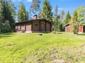 Une cabane en bois avec une cheminée, entourée d’une cour verdoyante et de grands arbres.