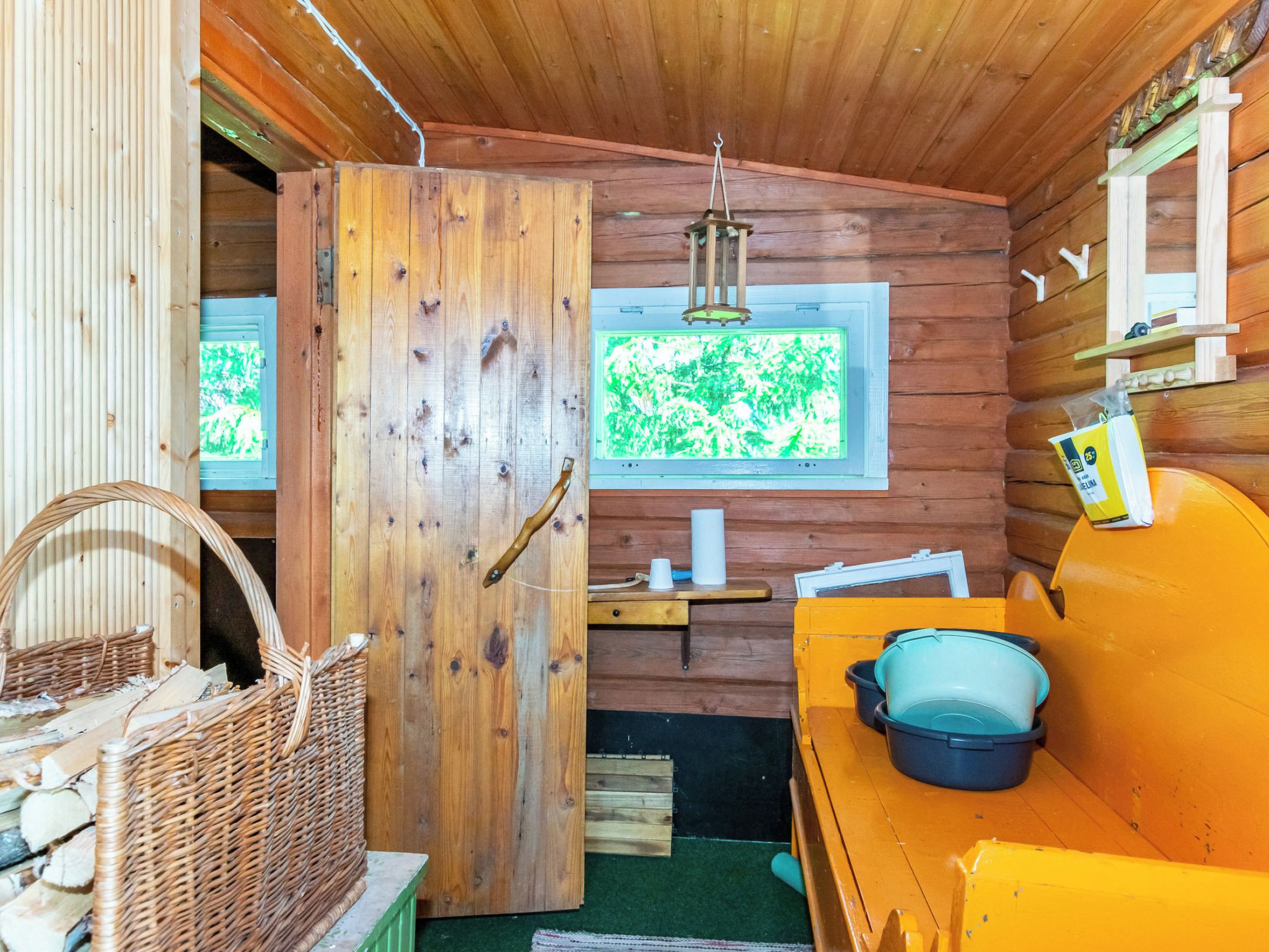 Interno accogliente di una baita rustica, con una porta in legno, una finestra vista e un divano giallo, più un cesto in vimini.