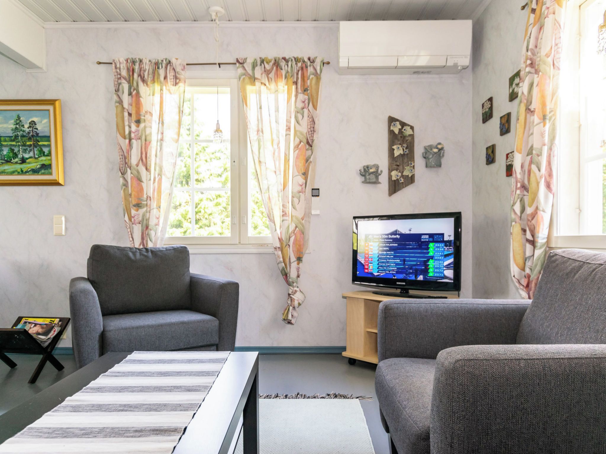 Una sala de estar con dos sofás grises, un televisor de pantalla plana y un cuadro en la pared.