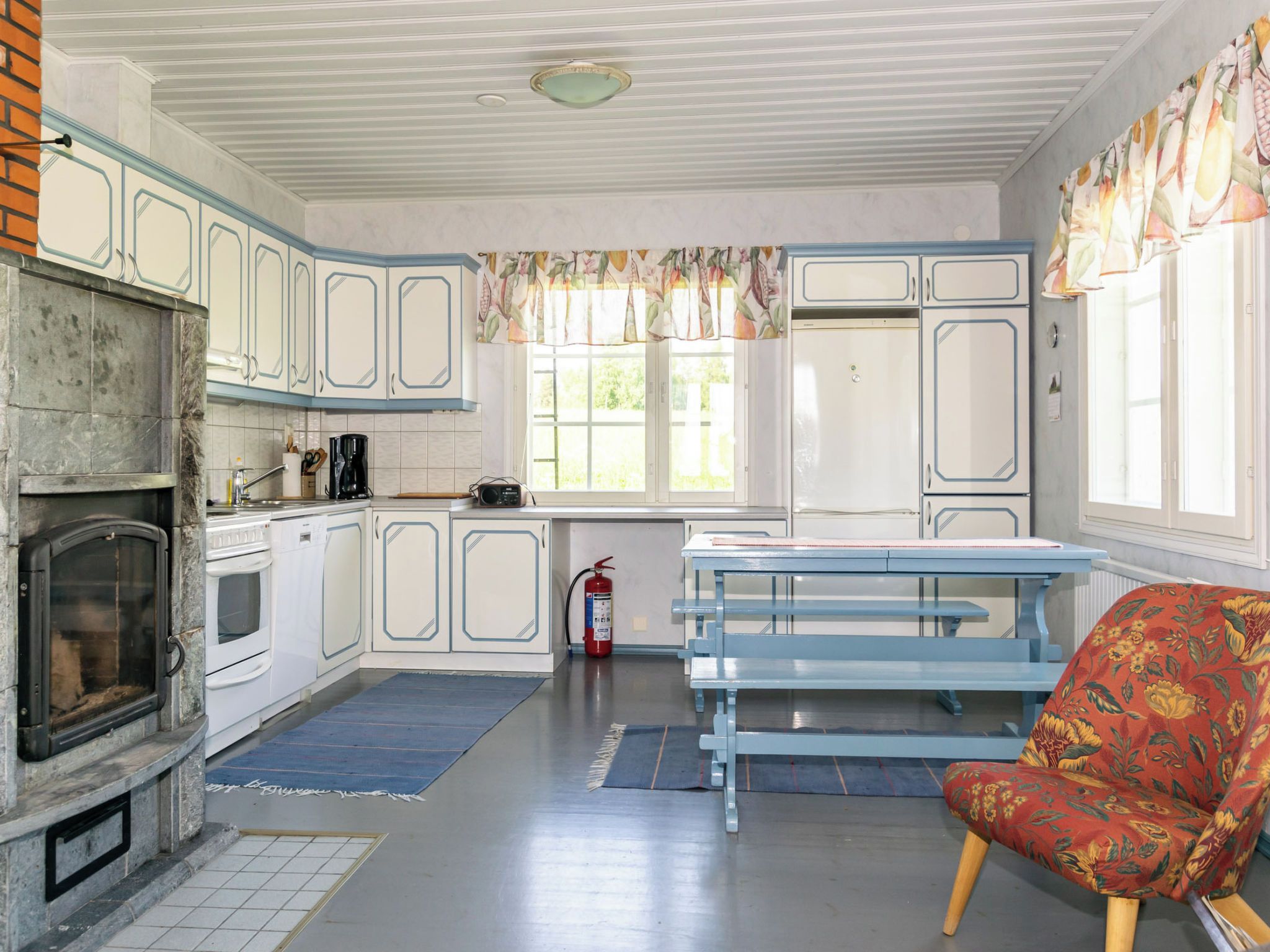 Een keuken met witte kasten, een inbouwoven, een koffiezetapparaat en een raam met gordijnen.