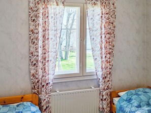 A room with a window, two beds, and a radiator.