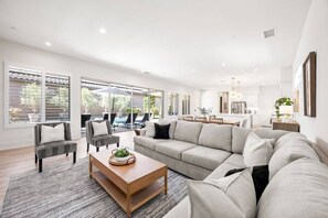 A spacious living area with a large sofa, a coffee table, and a dining area with chairs and a table. - Desert Jade: Pool, Spa, EV Charger, BBQ, and more! (La Quinta)