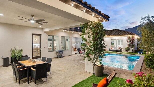Un patio exterior con piscina, zona de estar y ventilador de techo.