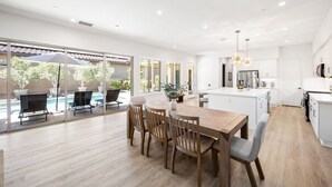 Una cocina moderna con armarios blancos, una isla central y un comedor con mesa y sillas de madera.