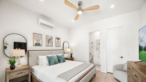 Un dormitorio con cama, mesitas de noche, ventilador de techo y televisión.