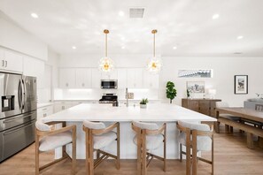 Une cuisine moderne dotée d’un îlot central, d’appareils électroménagers en acier inoxydable et de luminaires suspendus.