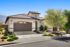 A single-story house with a brown garage door, a small attached garage, and a landscaped front yard with various shrubs and a tree.
